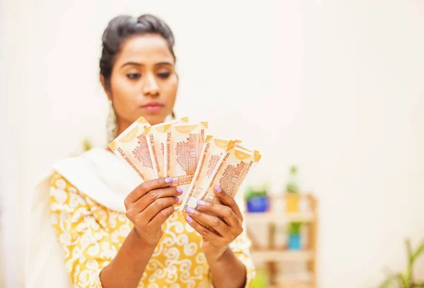 Concerned serious Indian woman counting money in Indian rupees at home