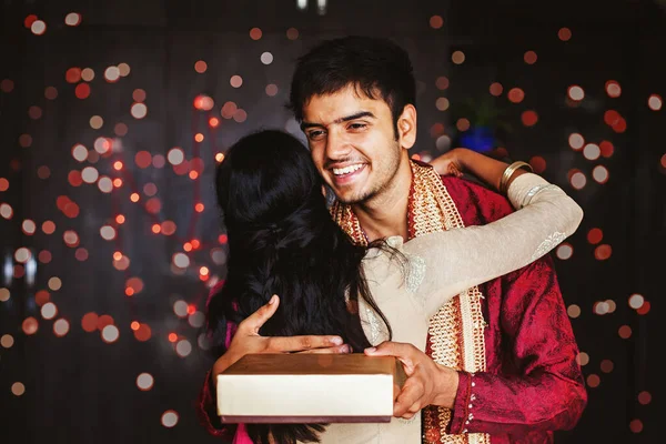 英俊潇洒的印度男子在家里用彩灯从一位年轻女子那里接过礼品盒 — 图库照片