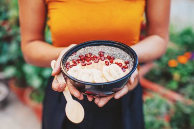 Elinde akai smoothie kasesi, nar, chia tohumu ve tahta kaşık tutan bir kadının yüzsüz fotoğrafı.