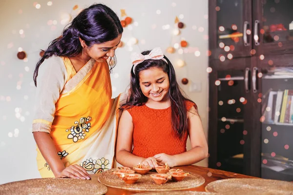 Cute little Indian girl lighting diyas for Diwali together with her mother at home