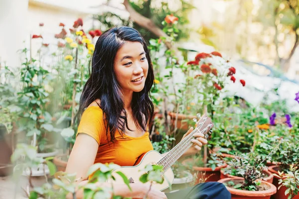 Junge Schöne Hongkongerin Spielt Ukulele Auf Ihrem Balkon Voller Blumentöpfe — Stockfoto