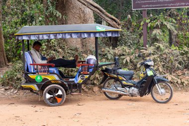 Siem Reap, Kamboçya - 01.05.2018; Tuk-Tuk sürücüsü istemcileri için gölgede bekler ve onun cep telefonu görünüyor