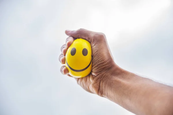 Hand squeeze yellow stress ball against the sky background