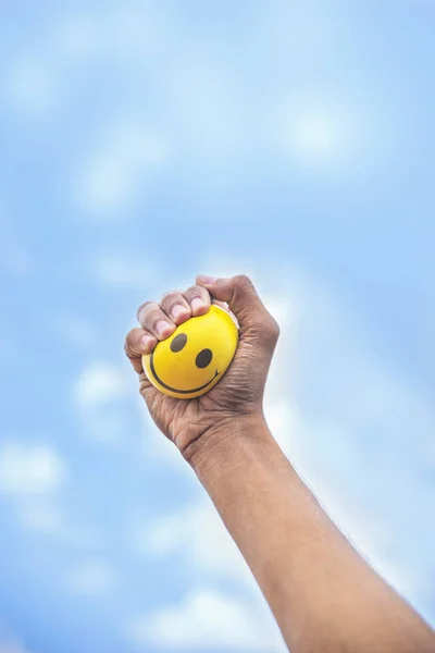 Hand squeeze yellow stress ball against the sky background