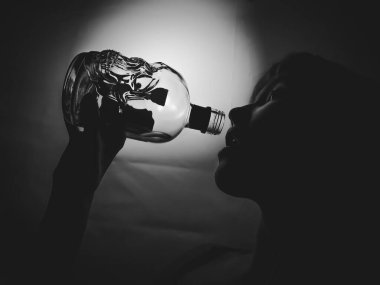 Kız zehirli sıvının son damlasını içiyor, kafatası şeklinde bir şişeden alkol içiyor. Işıklı arka planda siyah beyaz fotoğraf. Arkaplan