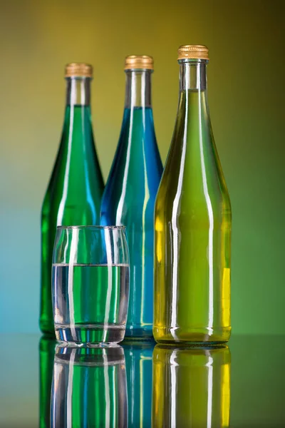 Een glas water en flessen op een kleurrijke achtergrond — Stockfoto