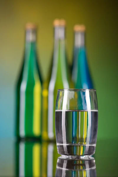 Een glas water en flessen op een kleurrijke achtergrond — Stockfoto