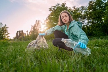 The girl collects trash from the forest in the trash bag