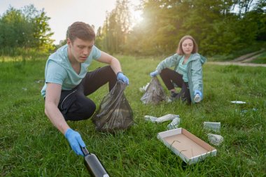 Plogging kavramı. Bir oğlan ve kız ormandan çöp topluyorlar. Çöp torbasında çöp topluyorlar.