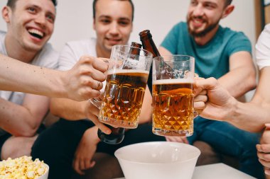 Cips patlamış mısır yerken ve soğuk bira içerken Tv izleyen arkadaşlar