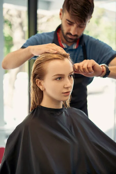 man hairdresser cuts hair of beautiful blonde woman