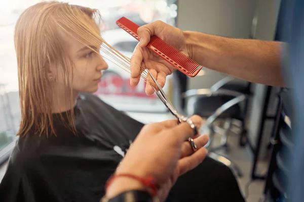 man hairdresser cuts hair of beautiful blonde woman