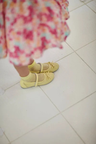 Menina em um vestido e em sandálias amarelas fica em uma telha branca — Fotografia de Stock