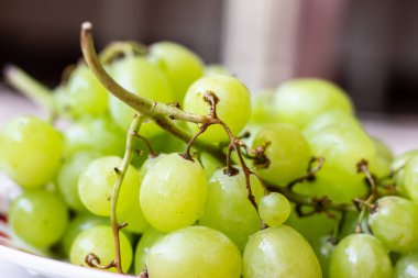 Beyaz ahşap masa üzerinde plaka olgun yeşil üzüm, üst görünümü. Masadaki tabakta yeşil üzümler. Masada kırmızı bir tabakta yeşil üzüm.