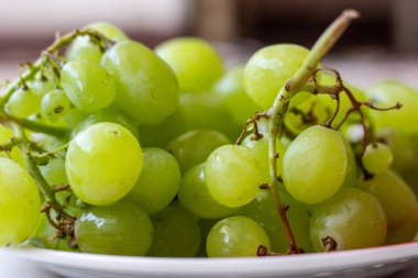 Beyaz ahşap masa üzerinde plaka olgun yeşil üzüm, üst görünümü. Masadaki tabakta yeşil üzümler. Masada kırmızı bir tabakta yeşil üzüm.