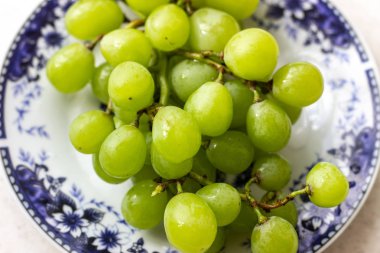 Beyaz ahşap masa üzerinde plaka olgun yeşil üzüm, üst görünümü. Masadaki tabakta yeşil üzümler. Masada kırmızı bir tabakta yeşil üzüm.