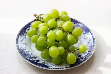 Beyaz ahşap masa üzerinde plaka olgun yeşil üzüm, üst görünümü. Masadaki tabakta yeşil üzümler. Masada kırmızı bir tabakta yeşil üzüm.