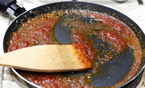 Κόκκινη σάλτσα από Αποξηραμένες ντομάτες στο τηγάνι. Ξύλινο φόντο, φύλλα βασιλικού και κόκκοι πιπεριού. Η ντομάτα τηγανίζεται σε τηγάνι. Ζεστό τηγάνι με ντομάτα — Φωτογραφία Αρχείου