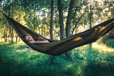 Ormanın ortasında hamakta dinlenen bir kadın gün batımını izliyor. Hayatın tadını çıkar, seyahat kampı konsepti