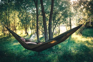 Ormanın ortasında hamakta dinlenen bir kadın gün batımını izliyor. Hayatın tadını çıkar, seyahat kampı konsepti