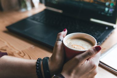 Öğrenci kadın iki eliyle bir bardak sıcak çay ve deniz dikenli su aygırı ve bir dilim portakal tutuyor. İş yeri, kalem ve dizüstü bilgisayarlı defter, çalışma süreci. Kahve dükkanı, mesaj için yer