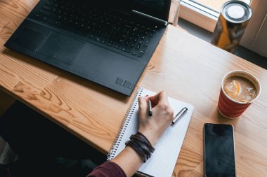 Kız küçük defterine, sıcak bir fincan çaya ve bir dilim portakala yazıyor. İş yeri, kalem ve dizüstü bilgisayarlı defter, çalışma. Kahve dükkanı, telefon, akıllı telefon masanın üstünde, eller, çalışma