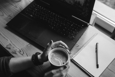 Üst Manzara. Öğrenci kadın iki eliyle su aygırı ve bir dilim portakallı çay tutuyor. İş yeri, kalem ve dizüstü bilgisayarlı defter, çalışma süreci. Kahve dükkanı, siyah ve beyaz.