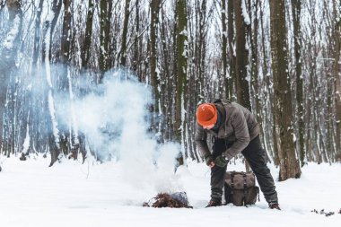 Gezgin adam ateş yakıyor. Kış zamanı. Açık havada macera tatili kavramı. Olağanüstü bir kamp. Antika sırt çantası ve termosla çay, karlı orman
