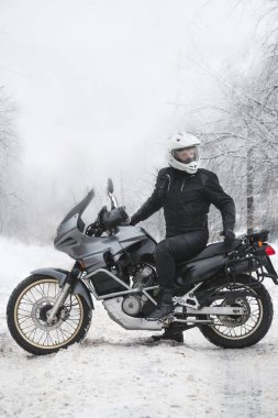 Sürücü adam macera motosikletinde oturuyor. Kış eğlencesi Karlı bir gün. Motosiklet ve kar. Enduro. off road dual spor seyahat turu, aktif yaşam tarzı konsepti. Kışlık giysiler, ekipmanlar, dikey fotoğraf