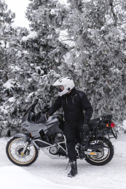 Sürücü adam macera motosikletinde oturuyor. Kış eğlencesi Karlı bir gün. Motosiklet ve kar. Enduro. off road dual spor seyahat turu, aktif yaşam tarzı konsepti. Kışlık giysiler, ekipmanlar, dikey fotoğraf