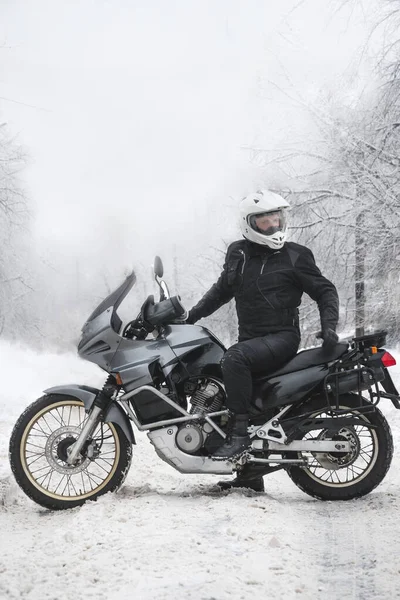 Sürücü adam macera motosikletinde oturuyor. Kış eğlencesi Karlı bir gün. Motosiklet ve kar. Enduro. off road dual spor seyahat turu, aktif yaşam tarzı konsepti. Kışlık giysiler, ekipmanlar, dikey fotoğraf