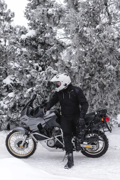Sürücü adam macera motosikletinde oturuyor. Kış eğlencesi Karlı bir gün. Motosiklet ve kar. Enduro. off road dual spor seyahat turu, aktif yaşam tarzı konsepti. Kışlık giysiler, ekipmanlar, dikey fotoğraf