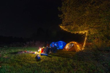 Turist kamp çadırı. Çelenkler, ışıklar. Vahşi bir yerde bir gece. Tatildeki insanlar. Aktif yaşam tarzı konsepti ve eğlence ve yürüyüş ekipmanları. Katlanan sandalyeler ve masa.
