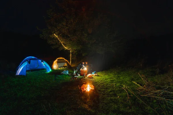 Tourist camping tent. garlands, lighting up. A night in a wilderness place. People on vacation. Active lifestyle concept and equipment for recreation and hiking. folding chairs and table. Bonfire fire