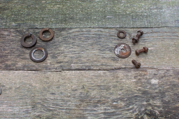 Weathered pallet wood boards as a background with 3 rusty washers placed in the upper left corner and separate nuts, bolts, and washers placed in the upper right corner.