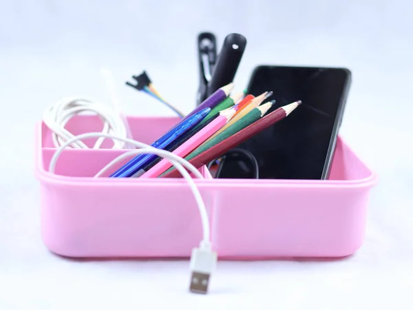 This image shows a pink desk organizer tray filled with various office supplies and electronic accessories.