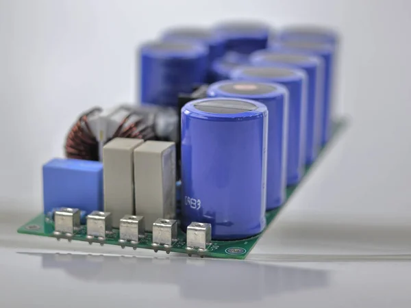 The image displays a circuit board populated with various electronic components, most prominently a row of large blue aluminum electrolytic capacitors