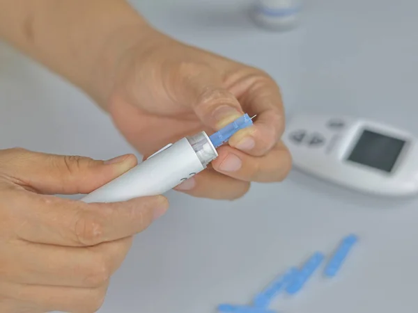 A close-up shot of a person's hands preparing a lancing device for a blood sugar test.