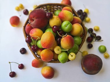 Beyaz zemin uzerinde, sepet icerisinde ve disinde seftali, kayisi, erik, kirmizi ve sari kirazlar 