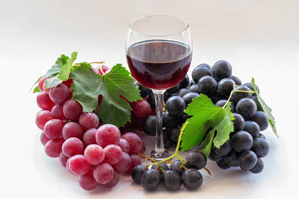 Red and black grapes on a white background and red wine in a glass