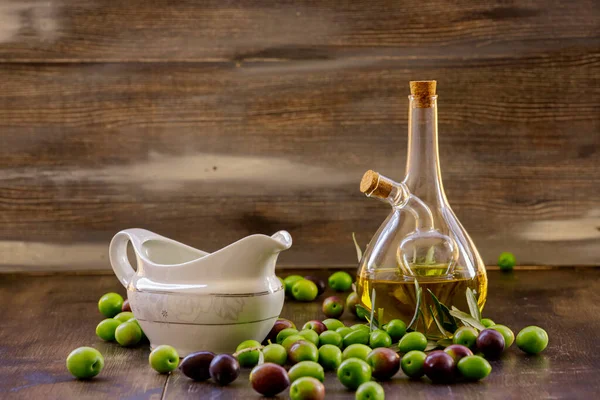 玻璃瓶中的橄榄油木制底座橄榄地面上的橄榄和一个白色的油锅 — 图库照片