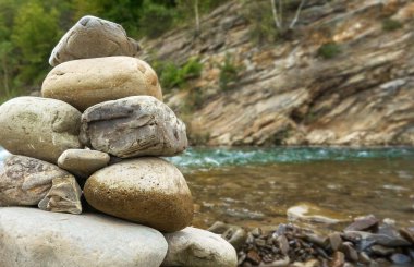 Nehirde akan suyun arka planına ve yeşil çimenli kıyıya yakın taş cairn. Taş nehir boyunca dengede duruyor. Seçici odak