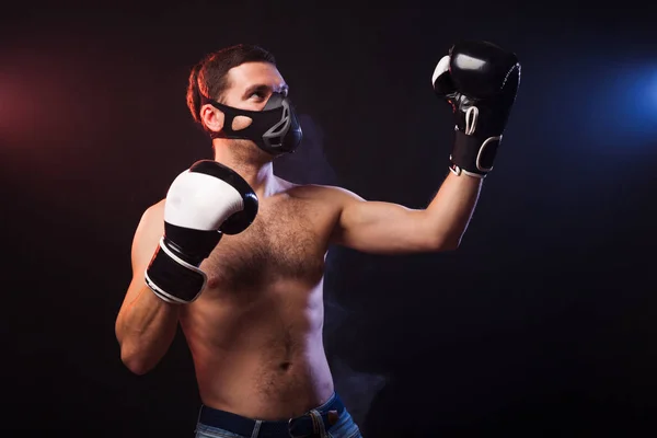 Winner of competitions. Studio portrait of a muscular boxer in professional gloves of European appearance with light bristles and hair on his chest. Smoke in the background is illuminated in blue and red