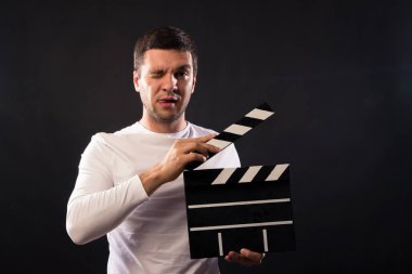 Genç adam beyaz görünüm bir Klaket tutuyor. Duman ve kırmızı ve mavi stüdyo ışık ile siyah bir zemin üzerine Studio'da portre vurdu. 