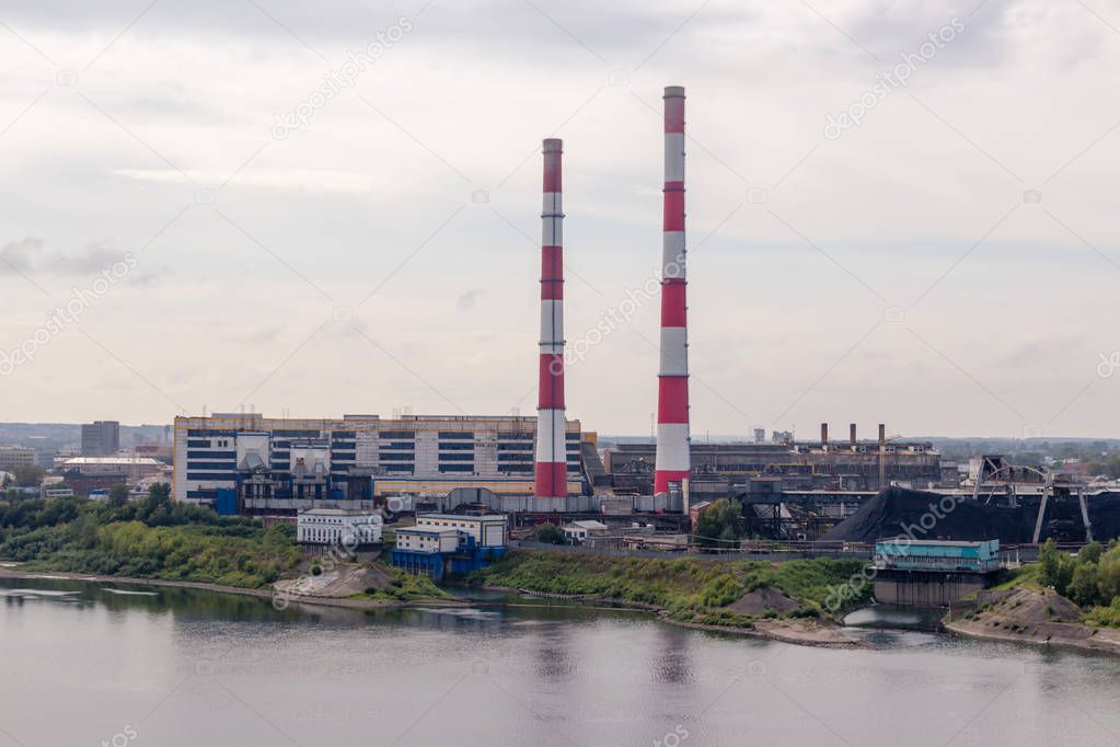 Coal processing plant operates on the river bank. The smoke from the pipes pollutes the atmosphere of the city. Concept of pollution of the environment, emissions into water resources. 