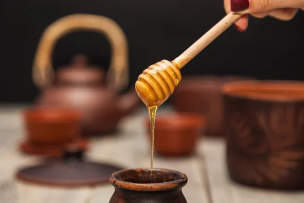 Tea ceremony, tea party. Clay dishes. Honey flows from a wooden spoon into a pot. Still life