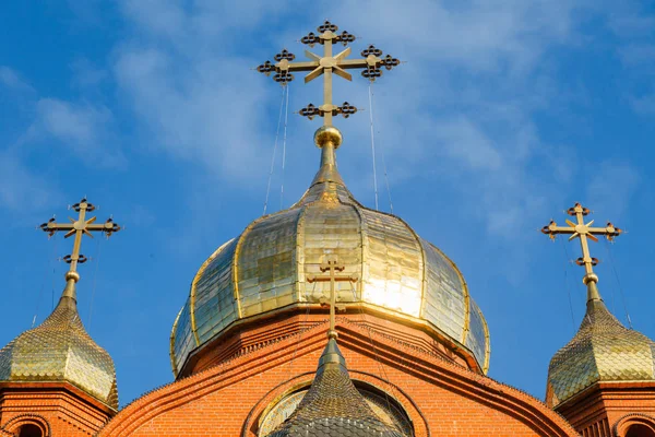 Old red brick Christian church with gold and gilded domes against a blue sky. Concept of faith in god, orthodoxy, prayer