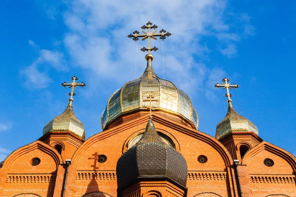 Old red brick Christian church with gold and gilded domes against a blue sky. Concept of faith in god, orthodoxy, prayer