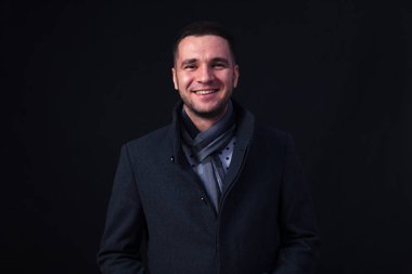 Studio bir siyah arka plan ve beyaz duman, kahverengi gözlü genç beyaz erkek esmer giyinmiş bir karanlık gri ceket ve kareli atkı. Soğuk hava kavramı, ağzından çıkan buhar, kış başlangıcı