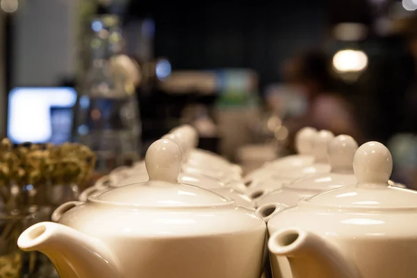 Many white ceramic teapots with round lids stand on the wooden bar counter in the restaurant. Concept dishes in cafe, tea, breakfast